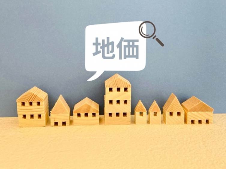 木製の家が並び「地価」の吹き出しと虫眼鏡