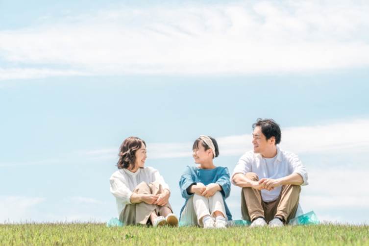 青空の下で芝生に座る三人家族の笑顔 