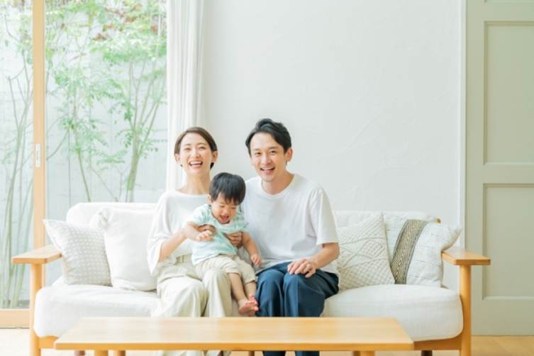 明るいリビングのソファで子どもを抱く夫婦  