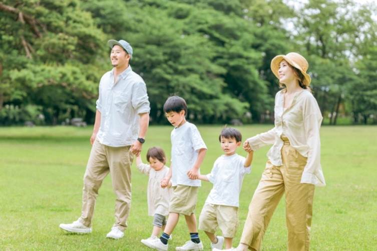 広い公園を手をつないで歩く五人家族  